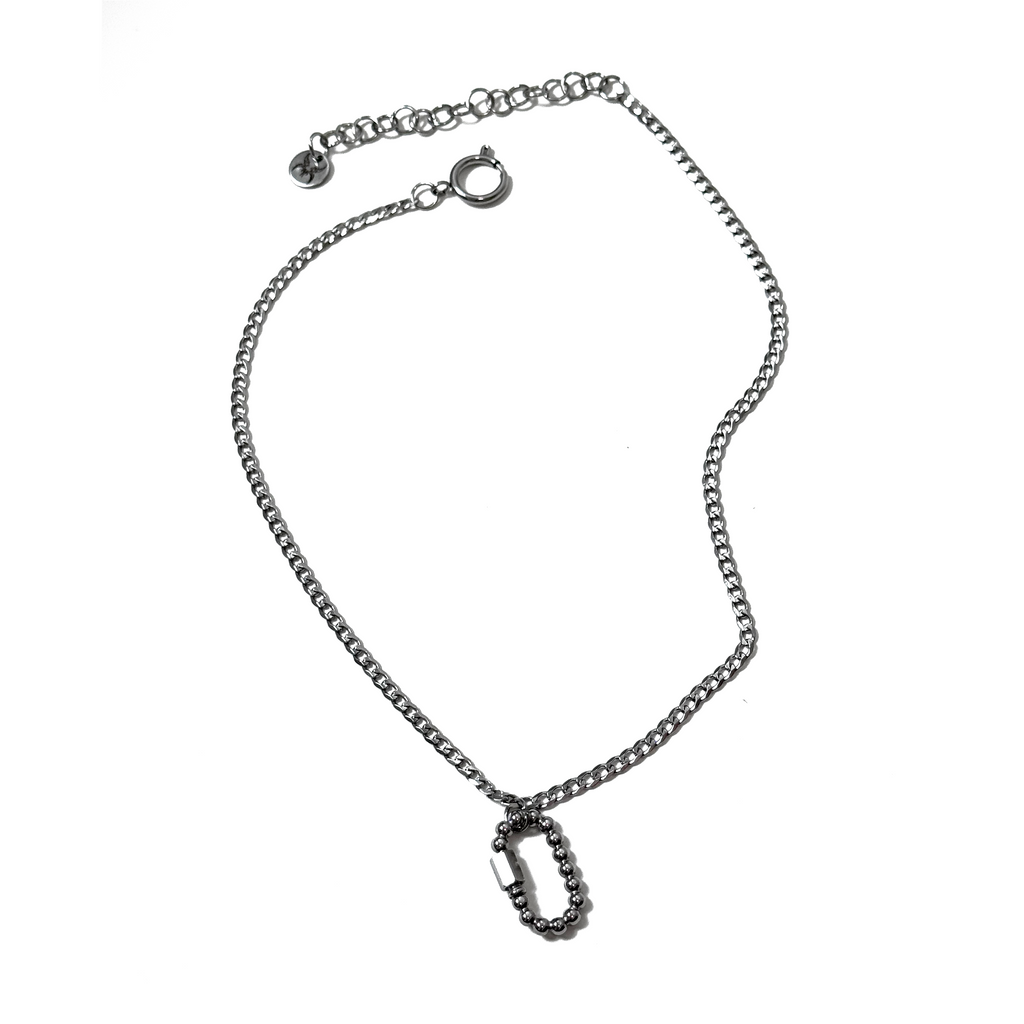 A silver-colored stainless steel necklace with a pearly carabiner clip, curb chain, and a signature fae engraved tag.