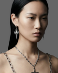Model wearing silver jewelry including earrings and a necklace on a gray background